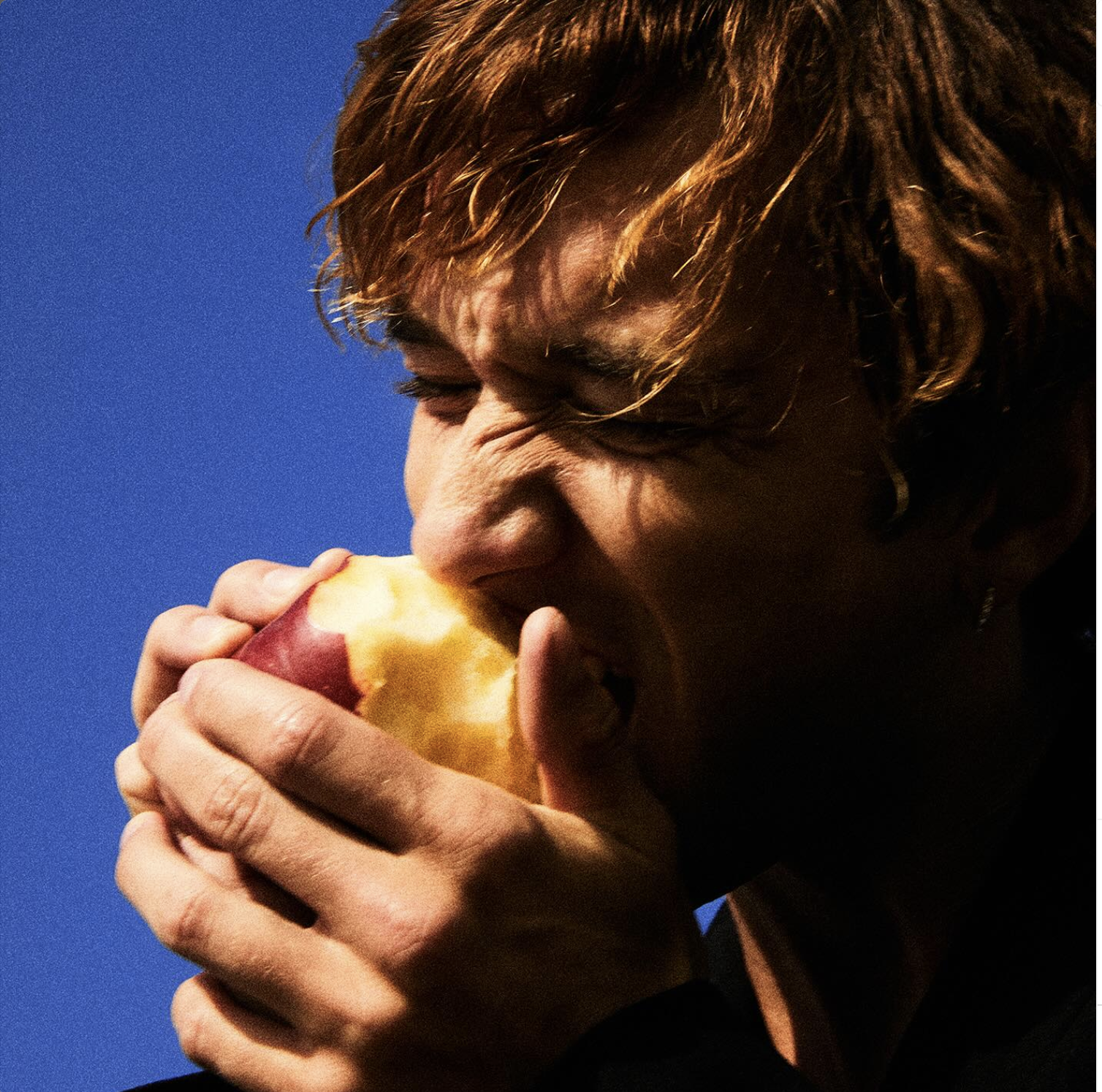 "Eden" single cover art. Daniel is eating an apple while showing the side of his face.